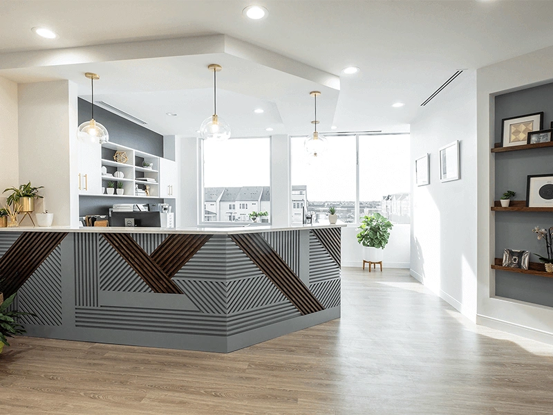 Modern dental office reception area with geometric front desk, pendant lighting, and warm wood flooring
